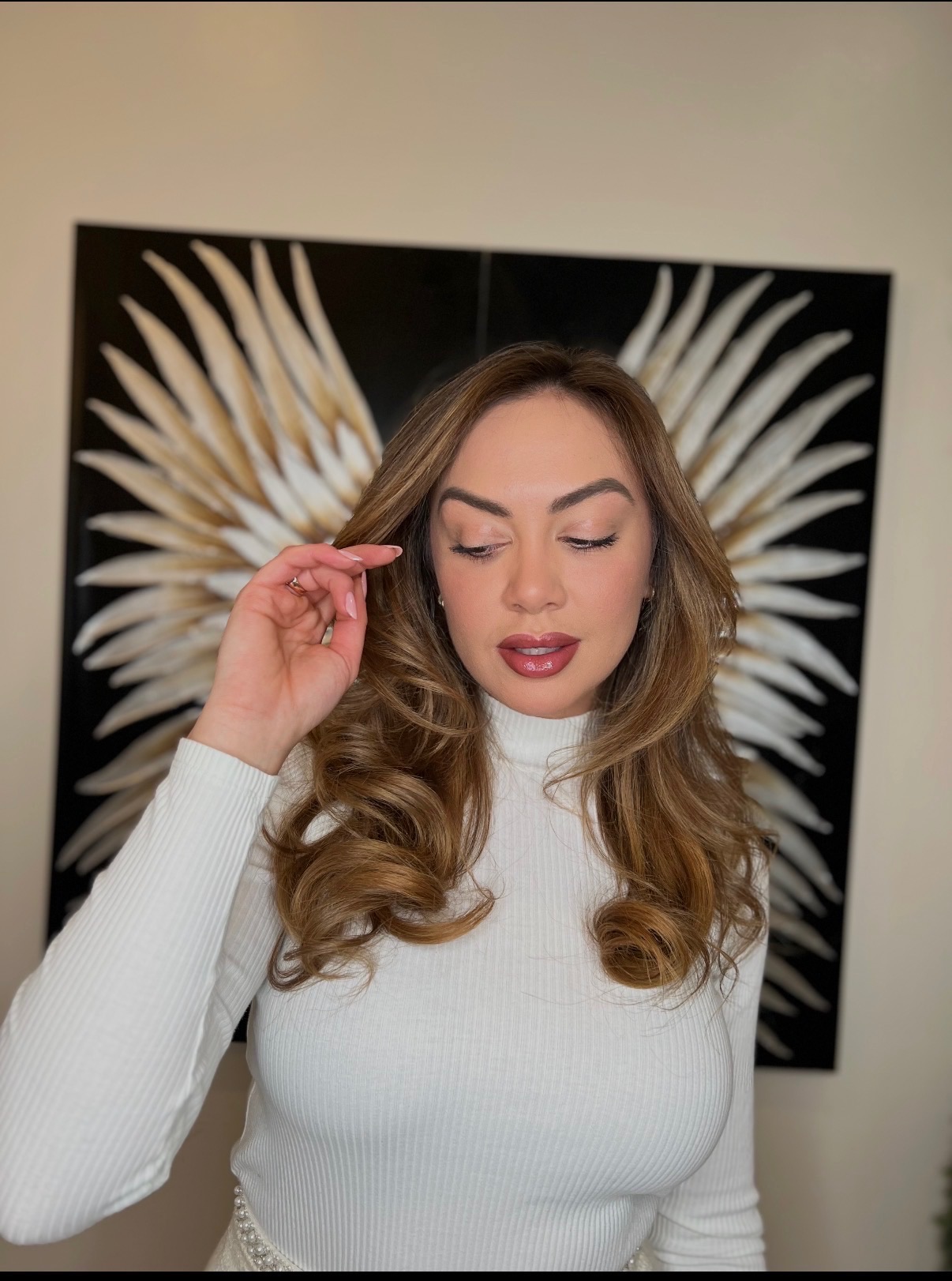 Soft caramel waves with face framing layers in front of the gold wings wall